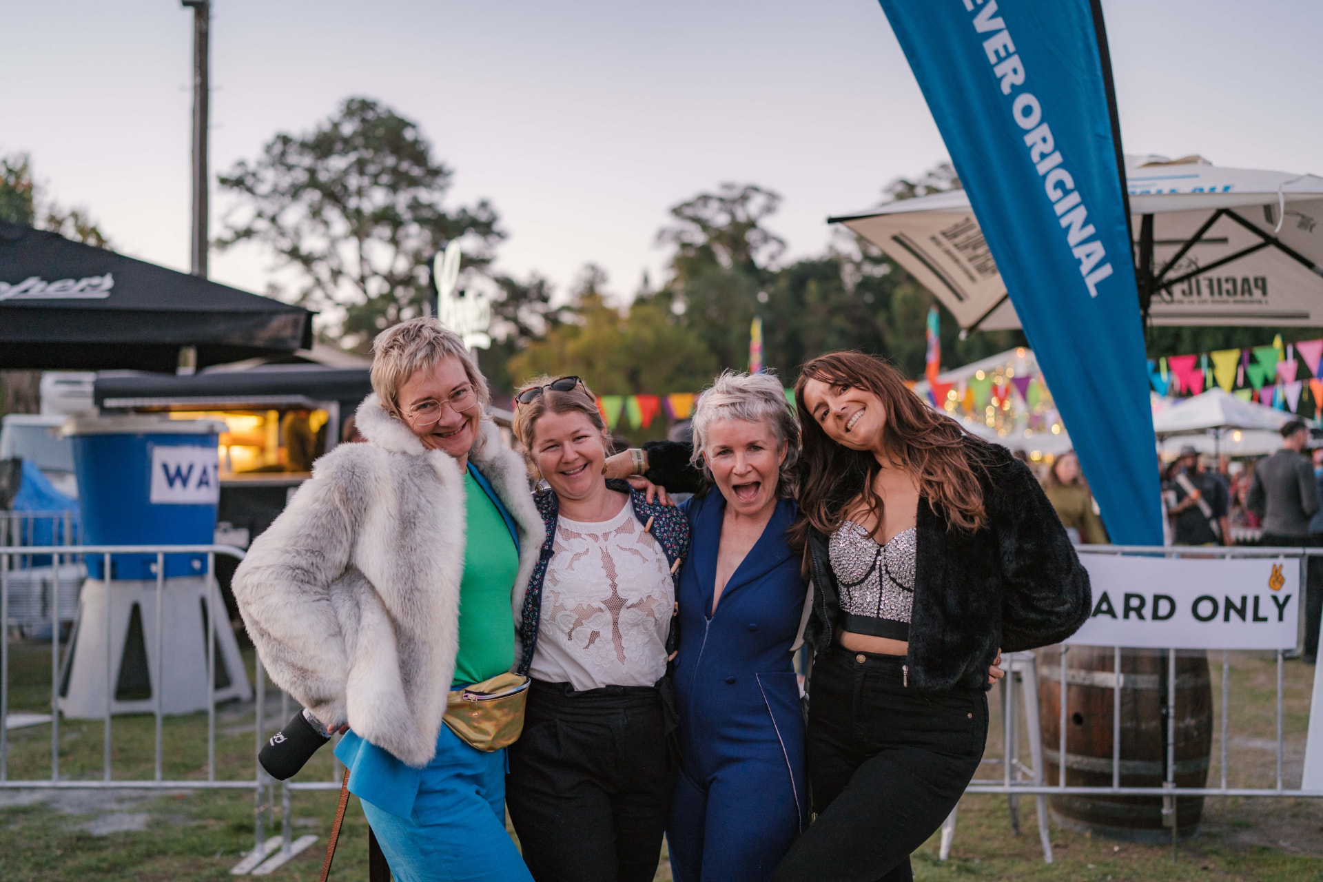 Four friends with arms around each other, laughing together at dusk