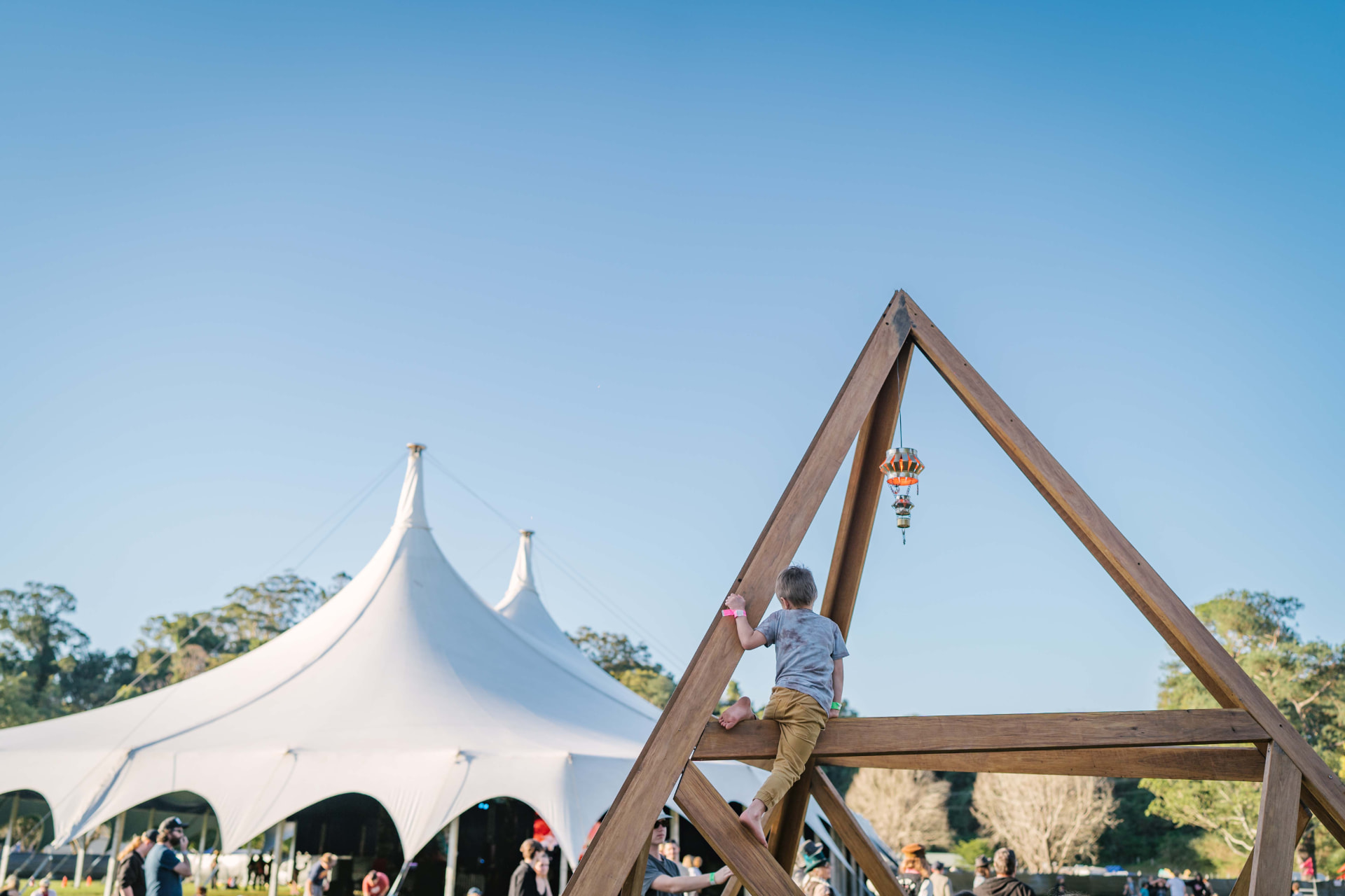 A child climbing an oversized triangular timber sculpture on the festival lawn